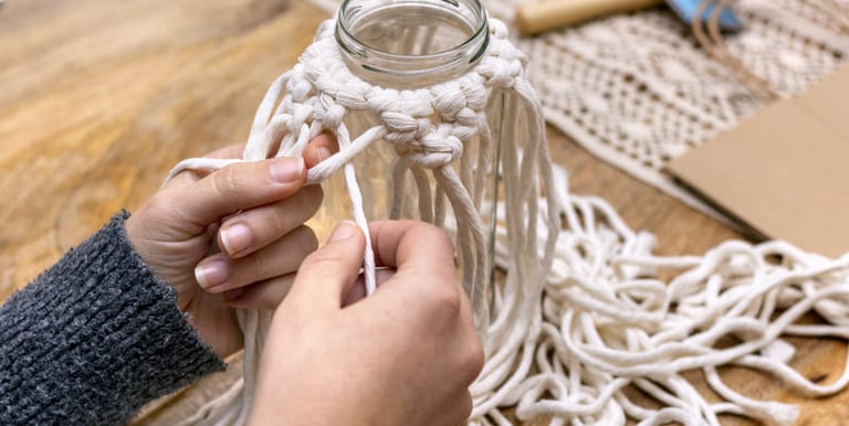 Manos practicando macramé en un frasco de vidrio.
