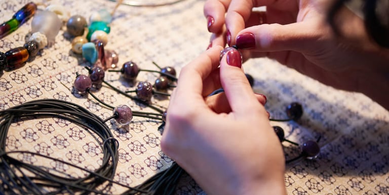 Manos de artesano colocando cuentas de vidrio artesanales en un cordón negro para crear un collar.