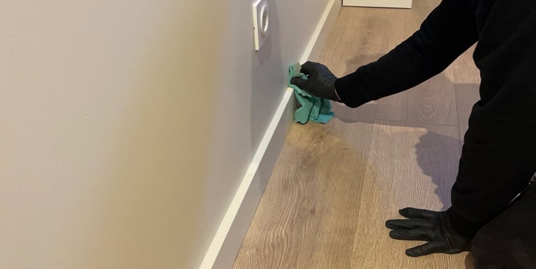 Nettoyage plinthes avec gants noir et chiffon vert sur parquet couleur bois
