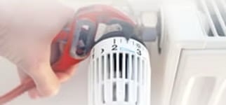 Plumber using a wrench to repair a radiator thermostat valve for home heating maintenance.