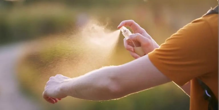 Una persona se aplica repelente de insectos en el brazo al aire libre, al atardecer.
