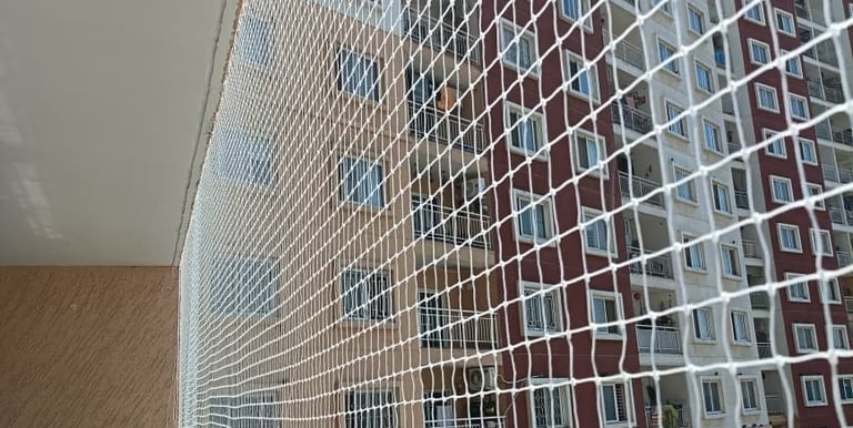 Worker carefully fitting a pigeon safety net on a residential balcony in bustling Mumbai.