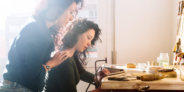 Dos artesanas trabajando juntas en un taller de macramé, rodeadas de herramientas 