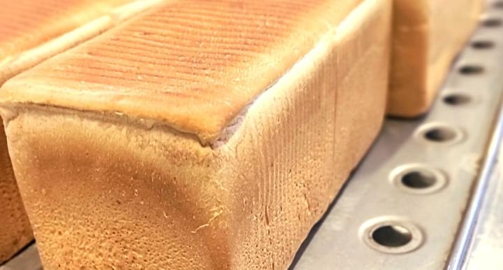 Freshly baked rectangular loaves of white sandwich bread cooling on a metal rack in a commercial bakery.