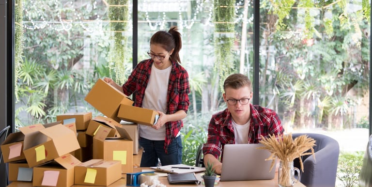 Shopify store owners managing orders and packing products while working on a laptop