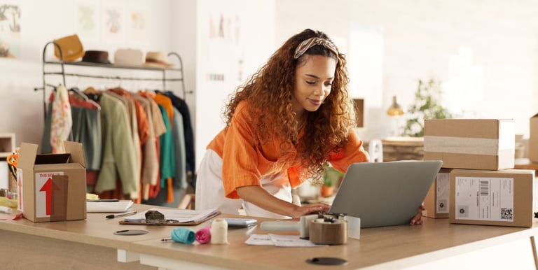 Female entrepreneur using a laptop to manage orders for her online clothing boutique shipping.