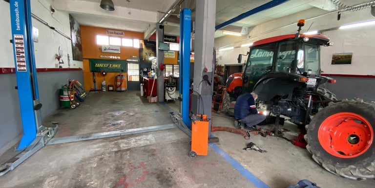 ένας μηχανικός τρακτέρ επισκευάζει ένα τρακτέρ με κουβούκλιο μέσα στο μεγάλο συνεργείο