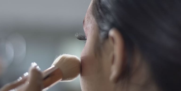 Maquilladora profesional aplicando polvos en el rostro de una mujer usando una brocha de contorno