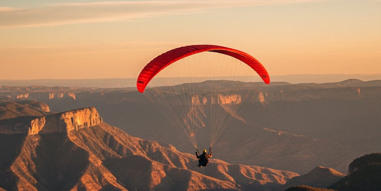A person paragliding with a red wing over mountain canyons during a golden sunset.