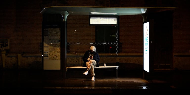 Homme penché sur son téléphone, assis à un arrêt de bus la nuit.
