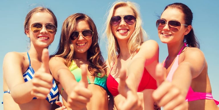 Group of four friends giving thumbs up at a fun Las Vegas dayclub pool party, enjoying the sunny day in colorful swimsuits