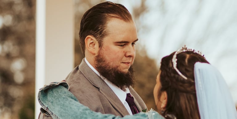 Groom in a grey suit and a bride in a denim jacket share a romantic moment during a gazebo wedding ceremony.