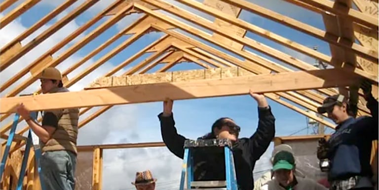 two women and a man framing the trusses of a house construction