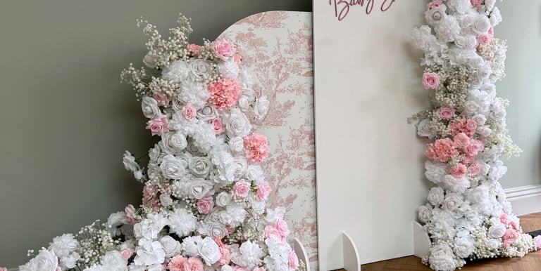 a large pink and white baby shower arch backdrop decorated with flowers