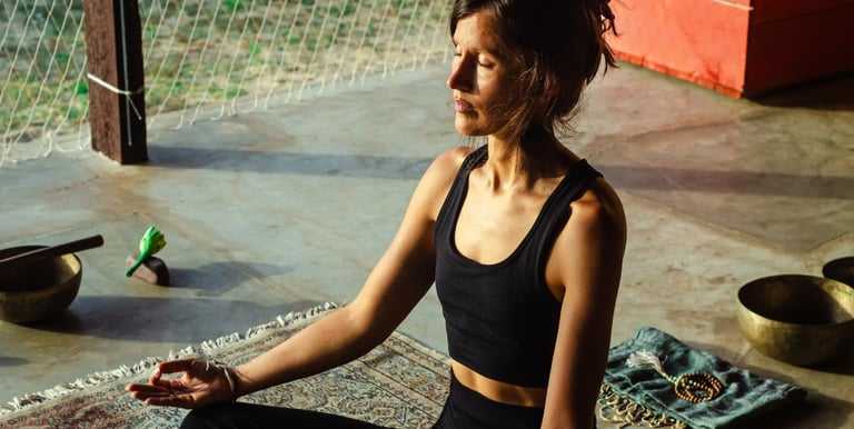Woman meditating on yoga mat in afternoon sun inside yoga shala, online meditation coaching