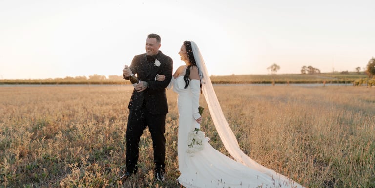 a bride and groom popping a champagne bottle at sunset