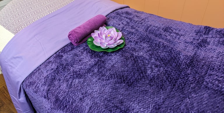 massage table with purple bedding and a lotus flower laying on top