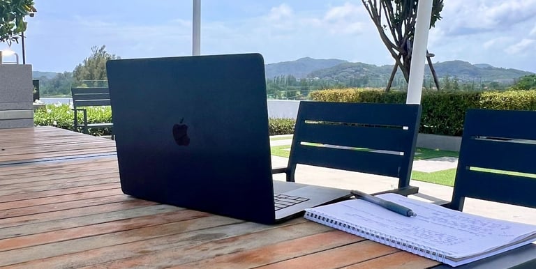A Mac Laptop on a table, with the mountains of Phuket in the background