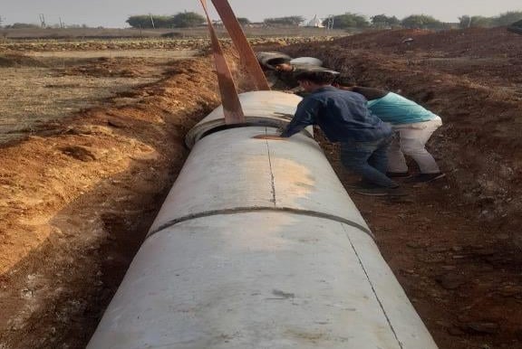 two people standing in a field with a large pipe pipe