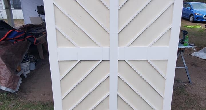 Custom white wooden sliding barn doors with a decorative chevron pattern outdoors.