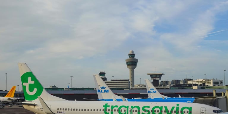 3 vliegtuigen van zowel Transavia als KLM op Schiphol met de verkeerstoren op de achtergrond