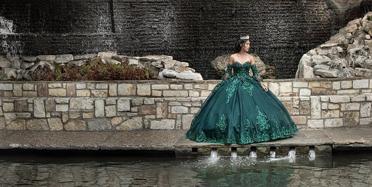 a woman in a green quinceanera dress standing in front of a waterfall