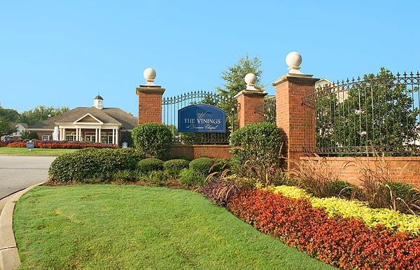 Brick entrance sign for The Vinings at Duncan Chapel apartment complex with manicured landscaping and a black iron fence.