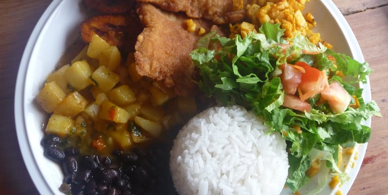 Traditional Casado plate with breaded fish, white rice, black beans, fried plantains, and fresh salad.