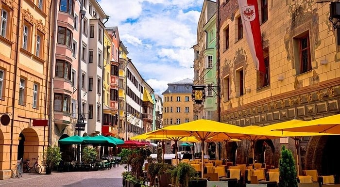 Colorful historic buildings and outdoor cafe tables with yellow umbrellas in Innsbruck Old Town, Austria.
