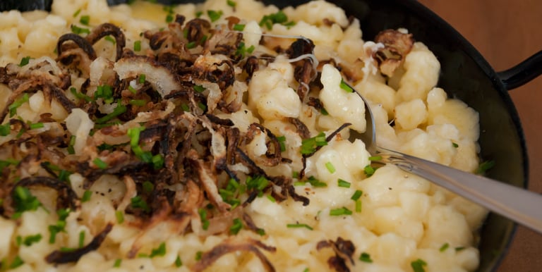 Traditional German Käsespätzle topped with crispy fried onions and fresh chives in a black pan.
