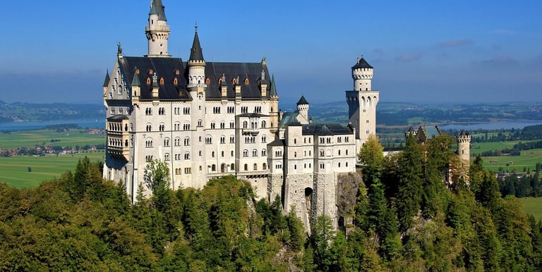 The Neuschwanstein Castle in Bavaria, Germany, stands on a rugged hill above a lush green forest.