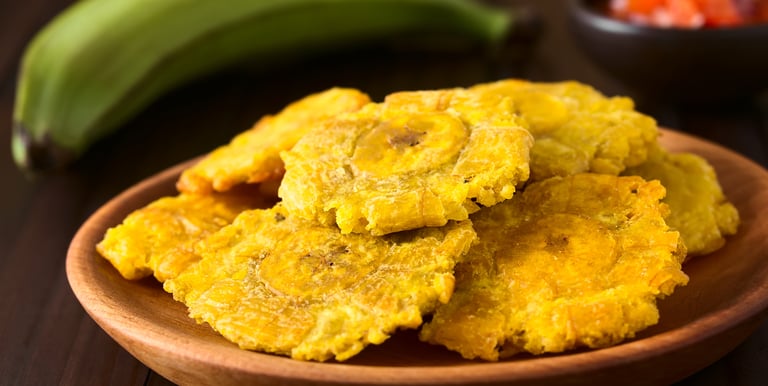 Crispy fried green plantains or tostones served on a wooden plate with a side of salsa.