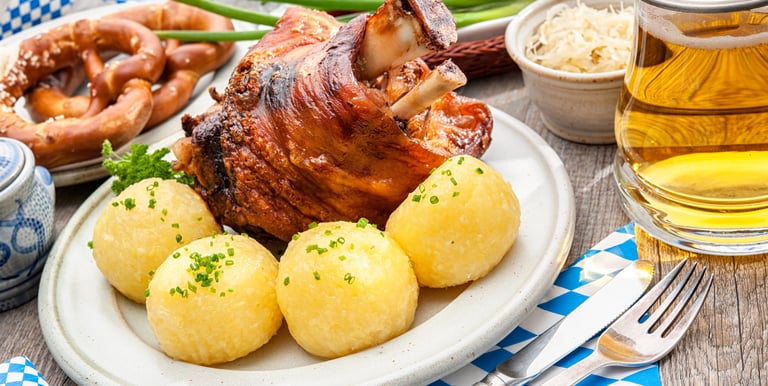 Roasted Bavarian pork knuckle served with potato dumplings, pretzels, and a glass of German beer.