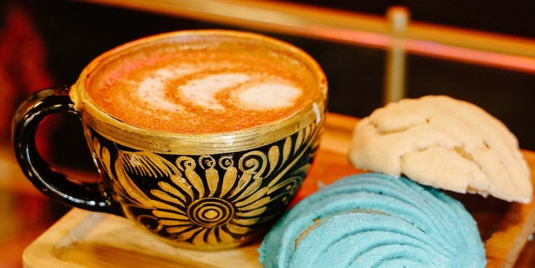 Mexican latte in an ornate black and gold cup served with colorful blue and white concha sweet bread.