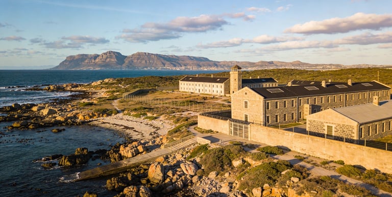 Aerial view of Robben Island Museum and prison buildings with Table Mountain in the background.