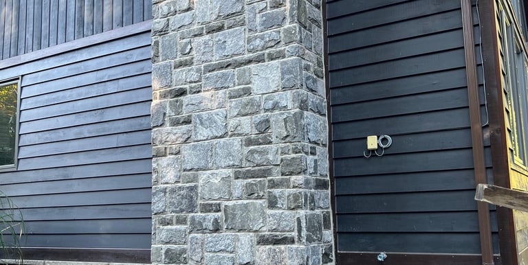 Rustic home exterior featuring a natural fieldstone chimney and dark wood siding.