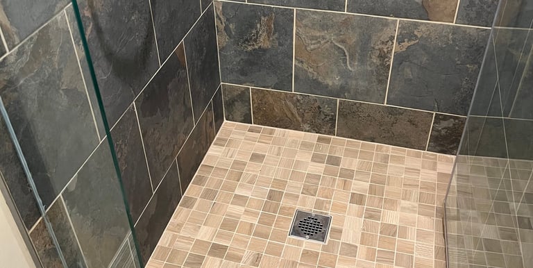 Walk-in shower with dark slate wall tiles, tan mosaic floor, and chrome fixtures.