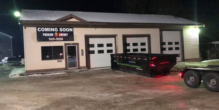 Pushaw Energy building at night with a large black dumpster parked in front of three white garage doors.