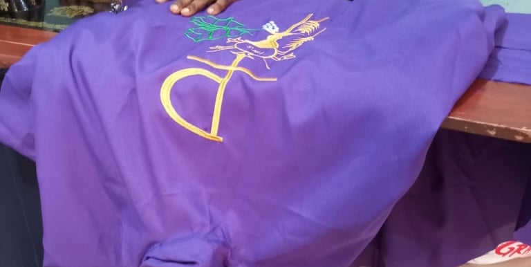 Tailor using a vintage sewing machine to embroider a gold religious symbol on purple liturgical fabric.