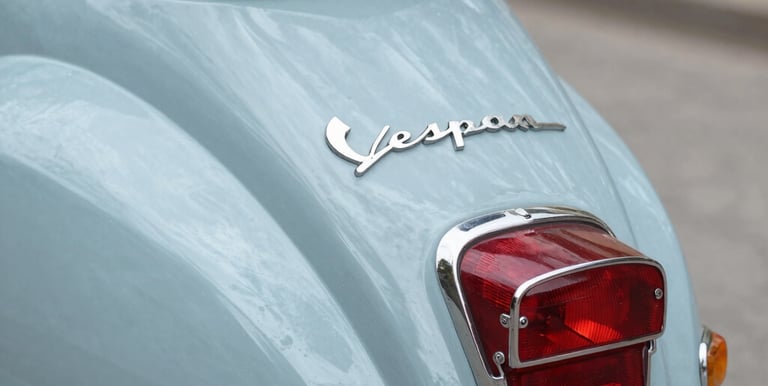 Classic electric Vespa parked on a cobblestone street with urban buildings in the background.