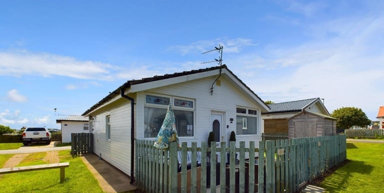 a small white bungalow chalet with a fenced in area