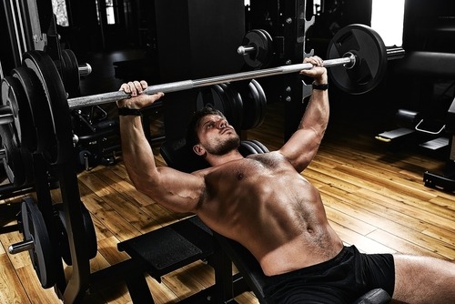 Muscular man performing an incline barbell bench press for chest strength training in a gym.