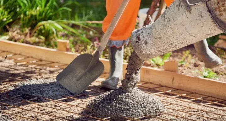 a person in orange pants and with a shovel pouring concrete