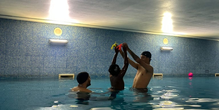 a Boy reaching for toys in the pool with 2 instructors