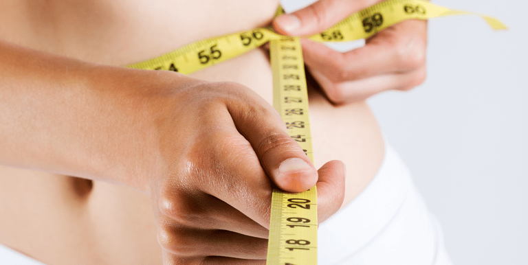 A woman measuring her waist with a measuring tape after receiving her mesotherapy treatment
