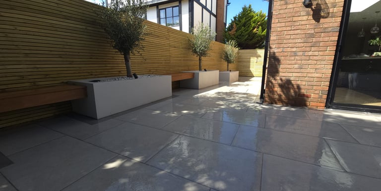 a porcelain patio with a planter and olive trees and a bench