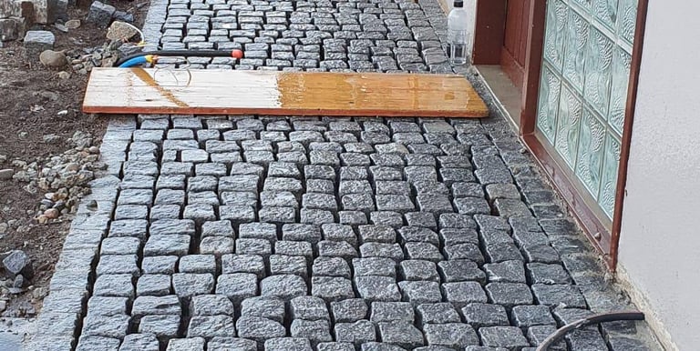 Natursteinplatten werden im Eingangsbereich verlegt – Werkzeuge und Holzplanke zeigen aktive Baustel