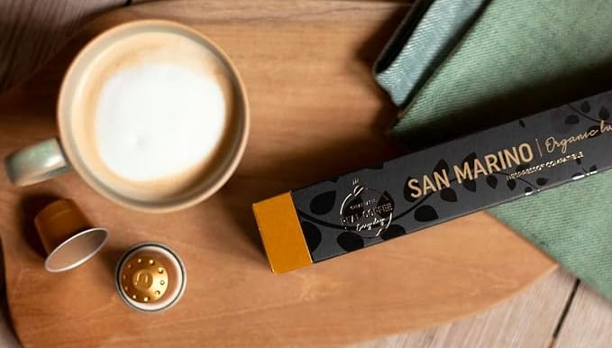 San Morino Real Coffee pods next to a latte on rustic table