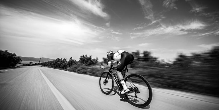 A cyclist in a low aerodynamic tuck riding a road bike on a paved highway under a wide sky.