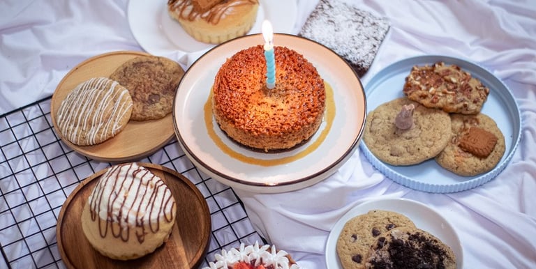 Postres gourmet surtidos, incluyendo un pastel de cumpleaños con vela encendida, galletas frescas